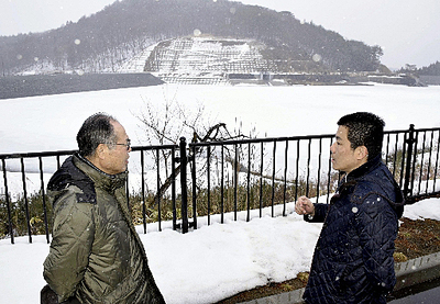 藤沼湖で森さん（左）から説明を受ける大内記者。左奥には新しくなった堤防が見える