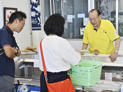 柴会長（右）からお薦めの魚介類の説明を聞く買い物客。県内外から県産魚介類を買い求める人が訪れた＝２４日正午、浪江町請戸・柴栄水産直売所