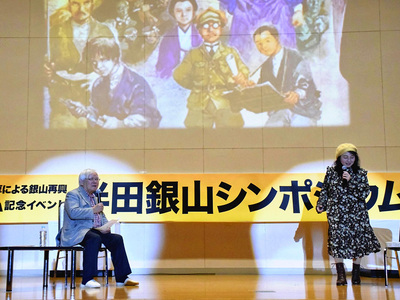 登壇した安彦さん（左）と佐々木さん。後ろのスライドは安彦さんが描いたイベントのポスターの一部。半田銀山で働いていた安彦さんの曽祖父の様子（スライド画像の右端）が描かれている＝１０日、桑折町