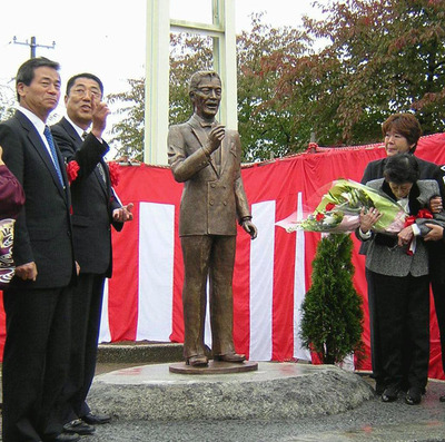 ＪＲ会津坂下駅前で行われた故春日八郎さんのブロンズ像の除幕式。春日さんの像と並んで立つ奥さま（右手前）と偲ぶ会の飯村孝男会長（左）ら。いろんな方の熱い思いが形になった